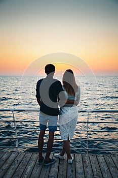 Young couple watching the sunrise at the beach, back view, seashore summer beach at yellow blue morning horizon sea