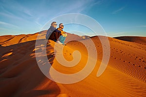 Young couple watching the sunrise on the sand dune in Sahara desert