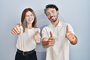 Young couple wearing casual clothes standing together approving doing positive gesture with hand, thumbs up smiling and happy for