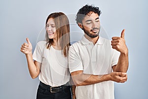 Young couple wearing casual clothes standing together looking proud, smiling doing thumbs up gesture to the side