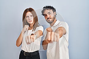 Young couple wearing casual clothes standing together punching fist to fight, aggressive and angry attack, threat and violence