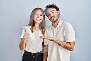 Young couple wearing casual clothes standing together showing palm hand and doing ok gesture with thumbs up, smiling happy and