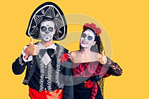 Young couple wearing mexican day of the dead costume over background doing happy thumbs up gesture with hand