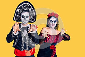 Young couple wearing mexican day of the dead costume over background smiling funny doing claw gesture as cat, aggressive and sexy