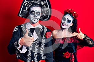 Young couple wearing mexican day of the dead costume over red doing happy thumbs up gesture with hand