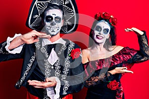 Young couple wearing mexican day of the dead costume over red gesturing with hands showing big and large size sign, measure symbol