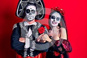 Young couple wearing mexican day of the dead costume over red happy face smiling with crossed arms looking at the camera