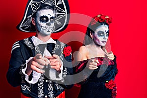 Young couple wearing mexican day of the dead costume over red pointing fingers to camera with happy and funny face
