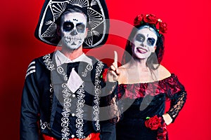 Young couple wearing mexican day of the dead costume over red showing and pointing up with finger number one while smiling