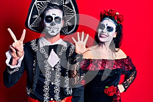 Young couple wearing mexican day of the dead costume over red showing and pointing up with fingers number seven while smiling
