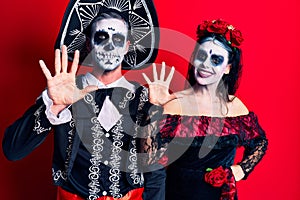 Young couple wearing mexican day of the dead costume over red showing and pointing up with fingers number ten while smiling