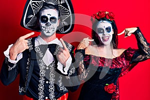 Young couple wearing mexican day of the dead costume over red smiling cheerful showing and pointing with fingers teeth and mouth