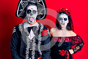 Young couple wearing mexican day of the dead costume over red sticking tongue out happy with funny expression