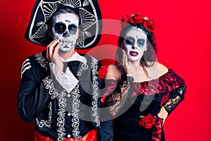 Young couple wearing mexican day of the dead costume over red touching mouth with hand with painful expression because of