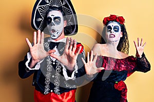 Young couple wearing mexican day of the dead costume over yellow afraid and terrified with fear expression stop gesture with
