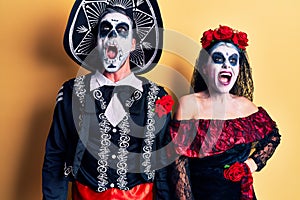 Young couple wearing mexican day of the dead costume over yellow angry and mad screaming frustrated and furious, shouting with