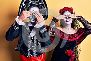 Young couple wearing mexican day of the dead costume over yellow covering eyes with hands smiling cheerful and funny