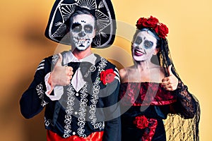 Young couple wearing mexican day of the dead costume over yellow doing happy thumbs up gesture with hand