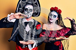 Young couple wearing mexican day of the dead costume over yellow gesturing with hands showing big and large size sign, measure
