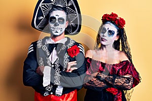 Young couple wearing mexican day of the dead costume over yellow happy face smiling with crossed arms looking at the camera