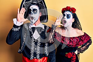 Young couple wearing mexican day of the dead costume over yellow shouting and screaming loud to side with hand on mouth