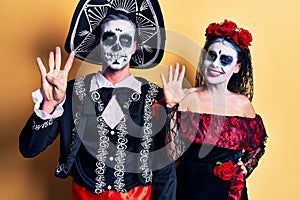 Young couple wearing mexican day of the dead costume over yellow showing and pointing up with fingers number nine while smiling
