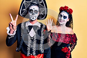 Young couple wearing mexican day of the dead costume over yellow showing and pointing up with fingers number seven while smiling