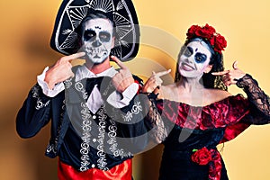 Young couple wearing mexican day of the dead costume over yellow smiling cheerful showing and pointing with fingers teeth and