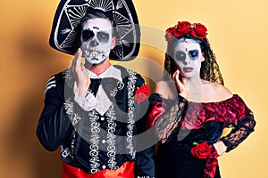 Young couple wearing mexican day of the dead costume over yellow touching mouth with hand with painful expression because of