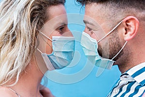 Young couple wearing protective face mask while staring on each other`s  eyes - Love and relationship during coronavirus time -