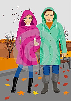 Young couple wearing raincoats standing in park in autumn photo