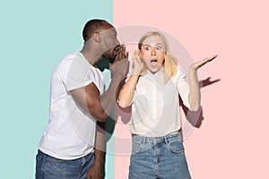 The young couple whispering a secret behind her hand over studio background