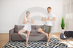 Young couple in white tshirts doing yoga at home standing in tree pose