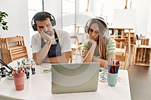 Young couple of wife and husband at art studio looking at video on laptop thinking looking tired and bored with depression