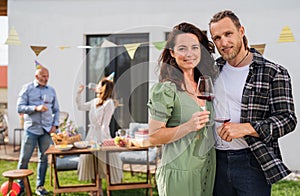 Young couple with wine outdoors in garden at home, birthday celebration party.