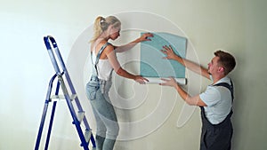 Young couple workers at construction site glues wallpaper to the wall