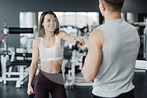 Young couple is working out at gym. Attractive woman and handsome muscular man trainer are training in light modern gym. Beautiful