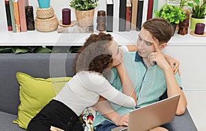 Young couples in love looking at each other on sofa with laptop in the living room