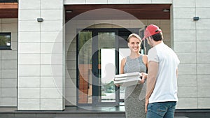 Young courier delivering pizza to luxury house. Smiling woman taking pizza boxes