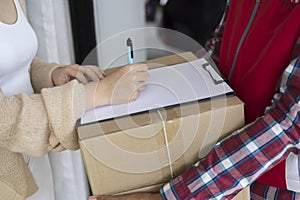 Young courier delivery man in red uniform holding a parcel cardboard box delivering package and woman putting signature in