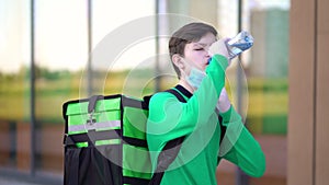 Young courier drinks water from a plastic bottle.