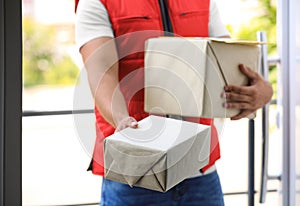 Young courier holding parcels on doorstep. Delivery service