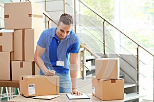 Young courier making notes on parcels at delivery department