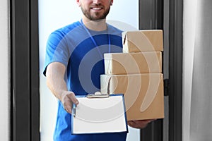 Young courier with parcels and clipboard indoors