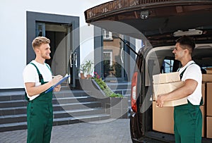 Young couriers with parcels near delivery car