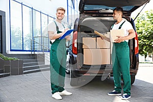 Young couriers with parcels near delivery car