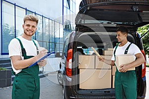 Young couriers with parcels near delivery car