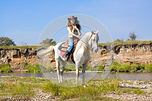 Young cowgirl on white horse at the river