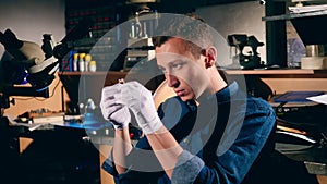 Young craftsman is observing a ring with a precious stone. Male silversmith is burning the frame of the silver ring