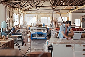 Young craftsman working on a laptop in his woodworking studio photo